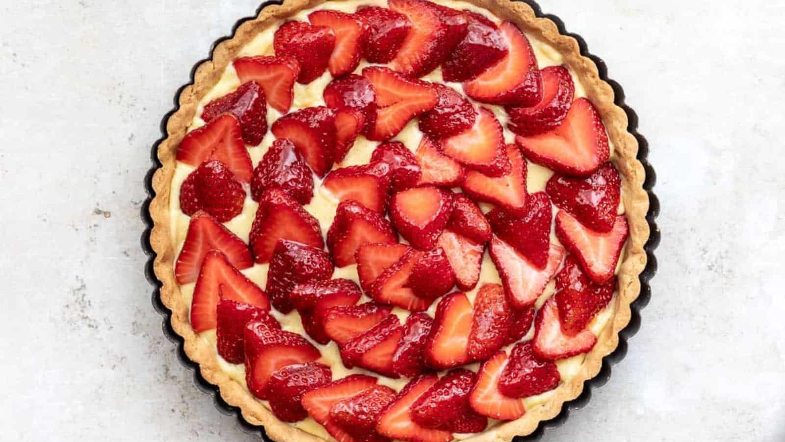A tart with a golden crust, creamy filling, and fresh sliced strawberries arranged on top.