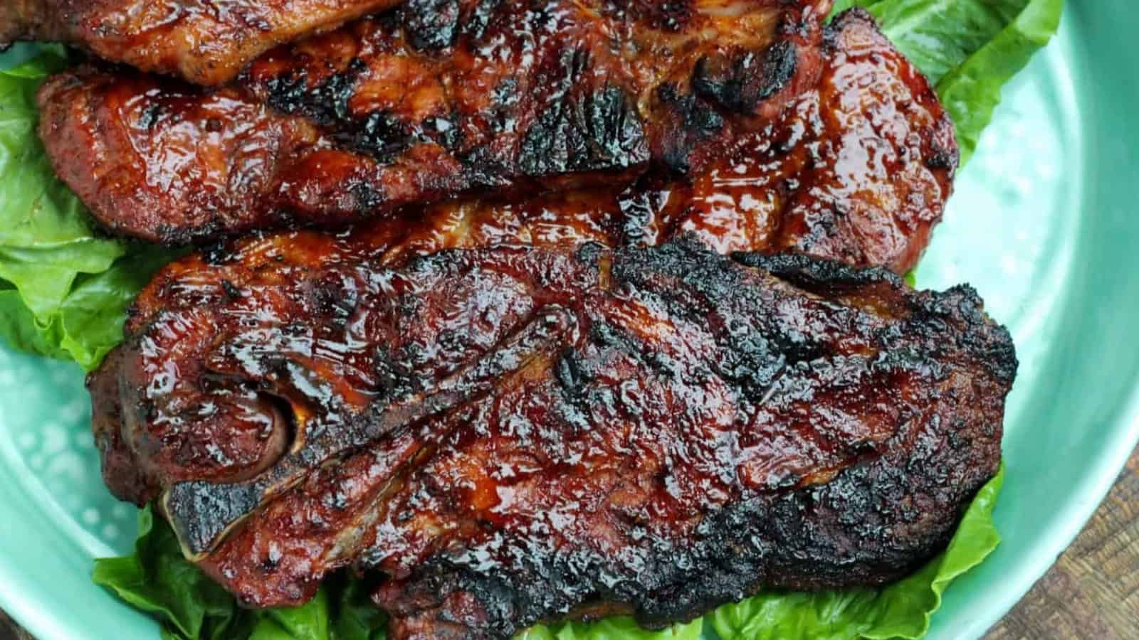Grilled, glazed pork steaks on a bed of fresh green lettuce on a light blue plate.