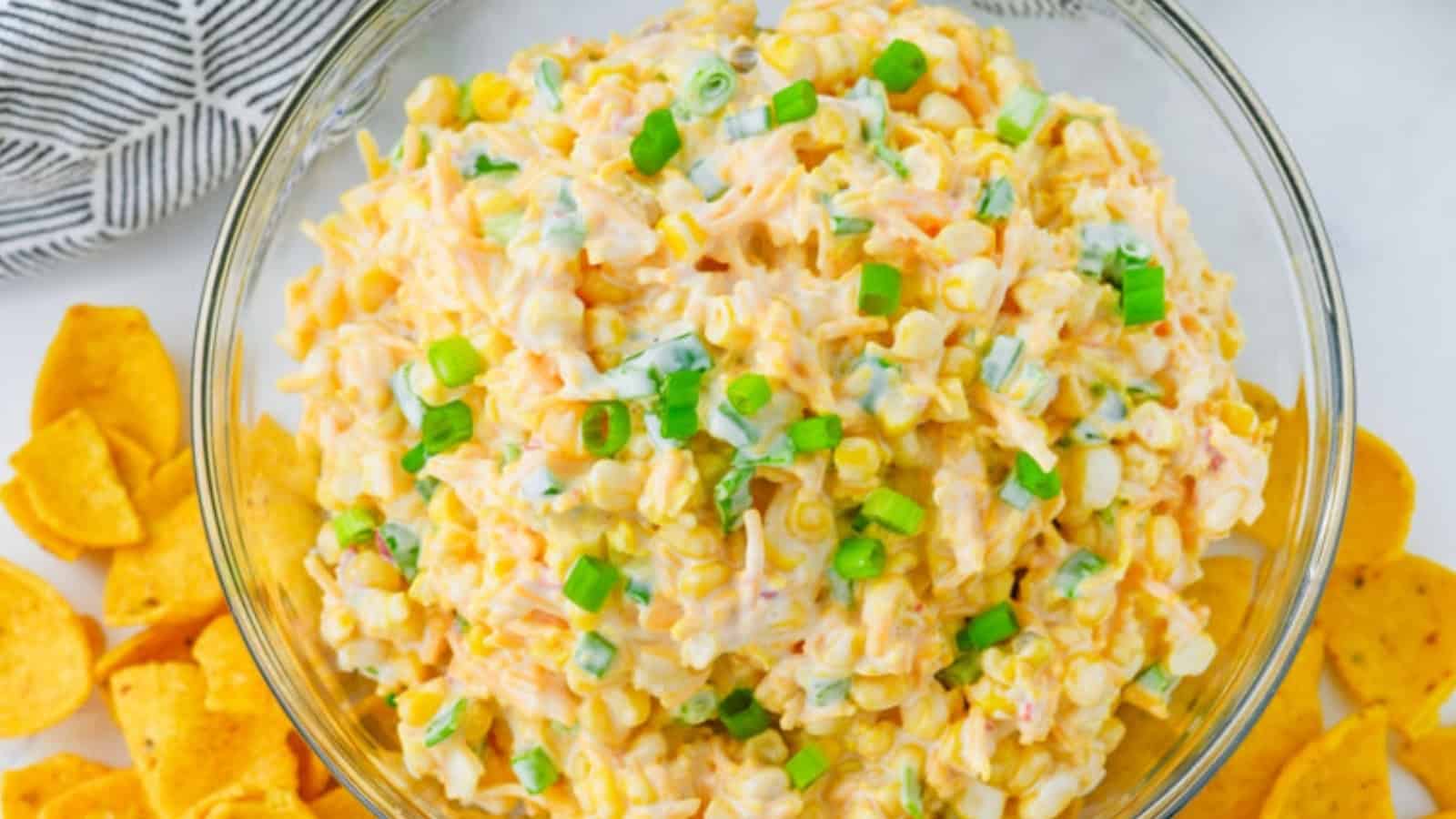 A bowl of creamy corn dip topped with chopped green onions, surrounded by corn chips.
