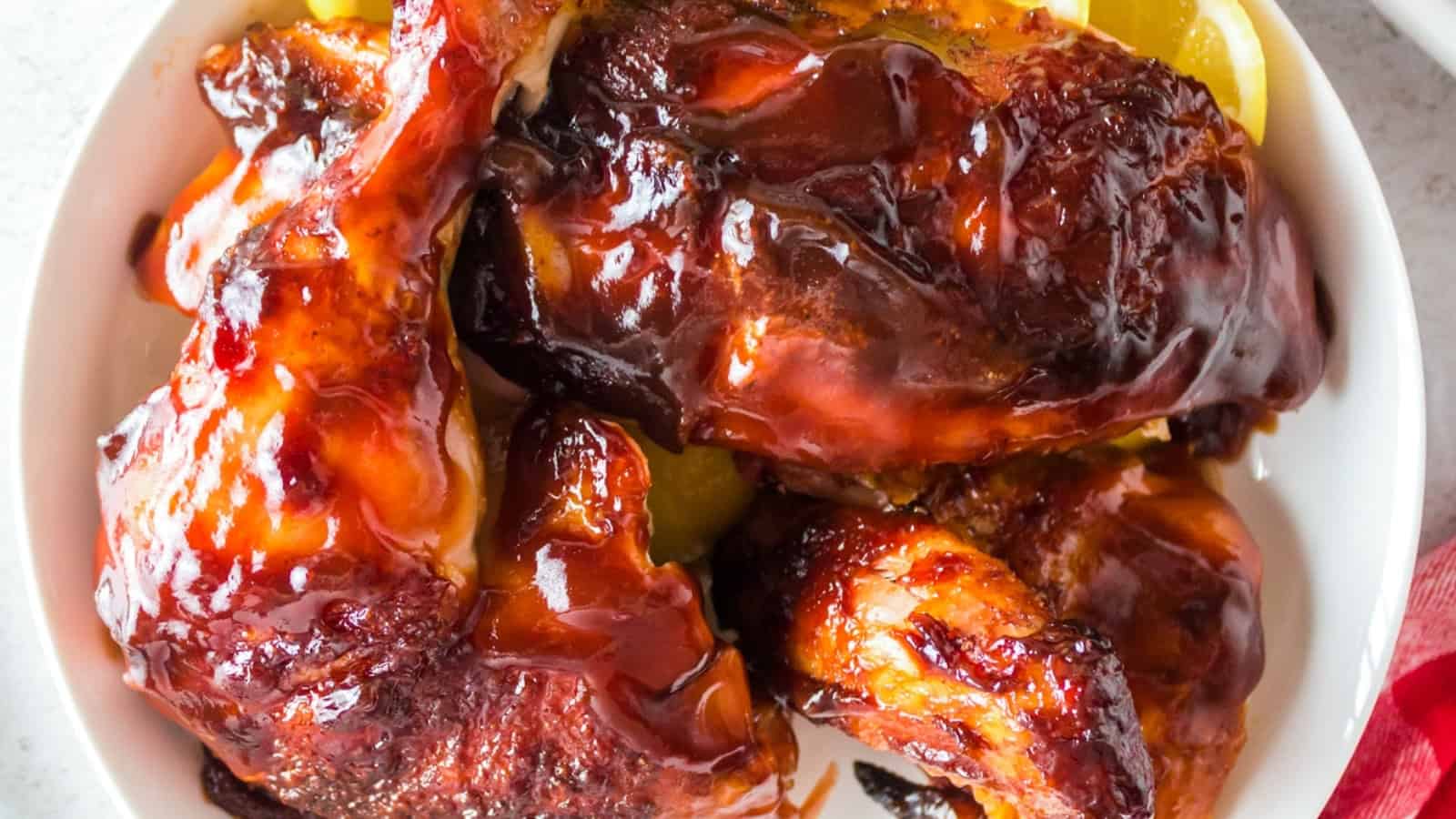 Barbecue chicken pieces glazed with sauce, served on a white plate with some yellow pickle slices.