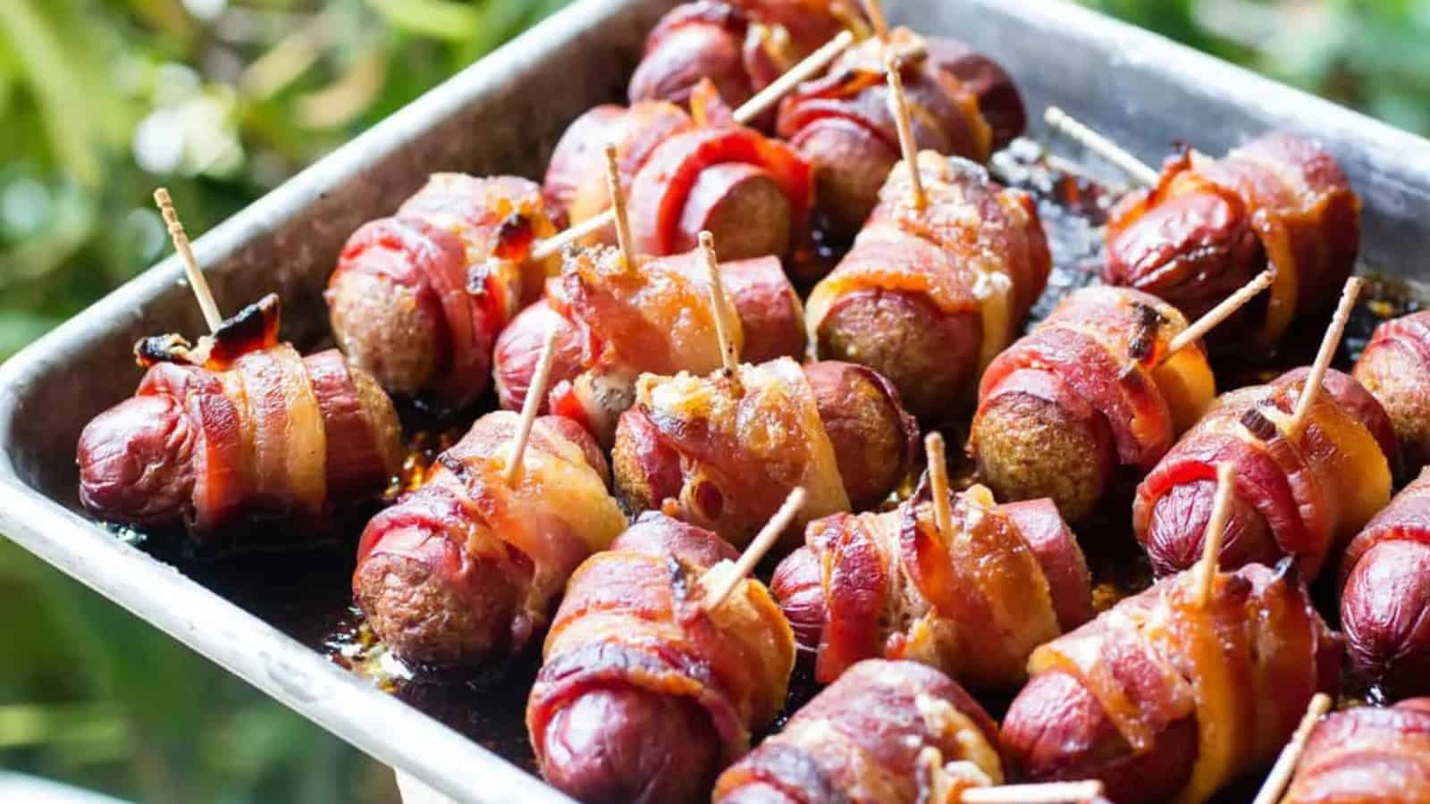 Bacon-wrapped sausages on a baking tray, each secured with a toothpick and cooked until crispy.