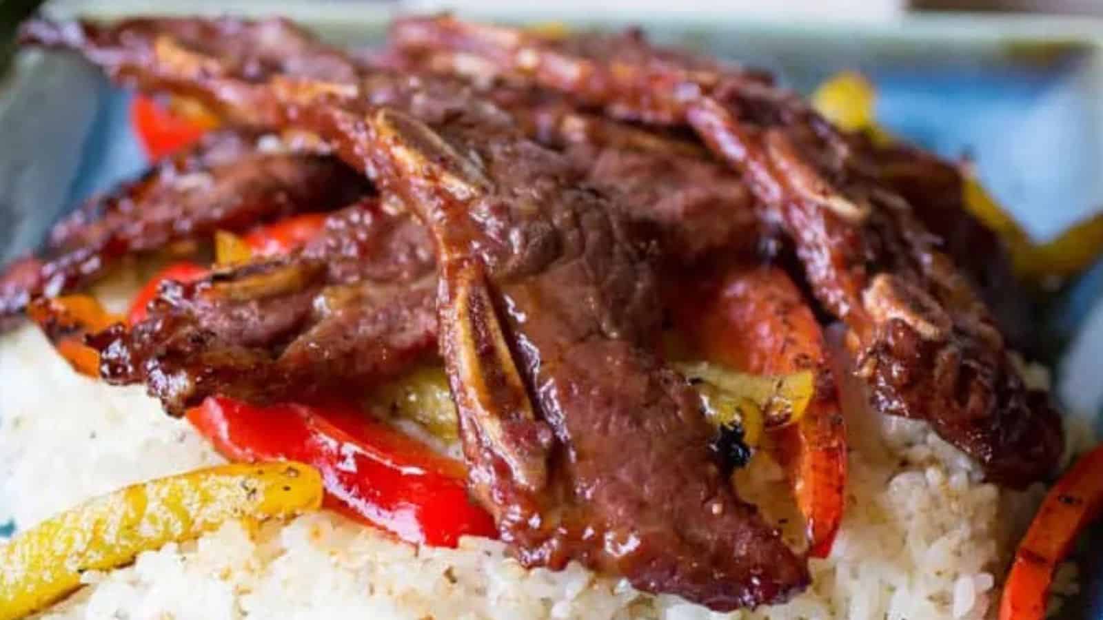 Grilled beef short ribs on a bed of white rice with saut&eacute;ed red and yellow bell peppers.