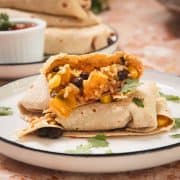 A burrito with rice, beans, corn, and vegetables on a plate, garnished with cilantro.