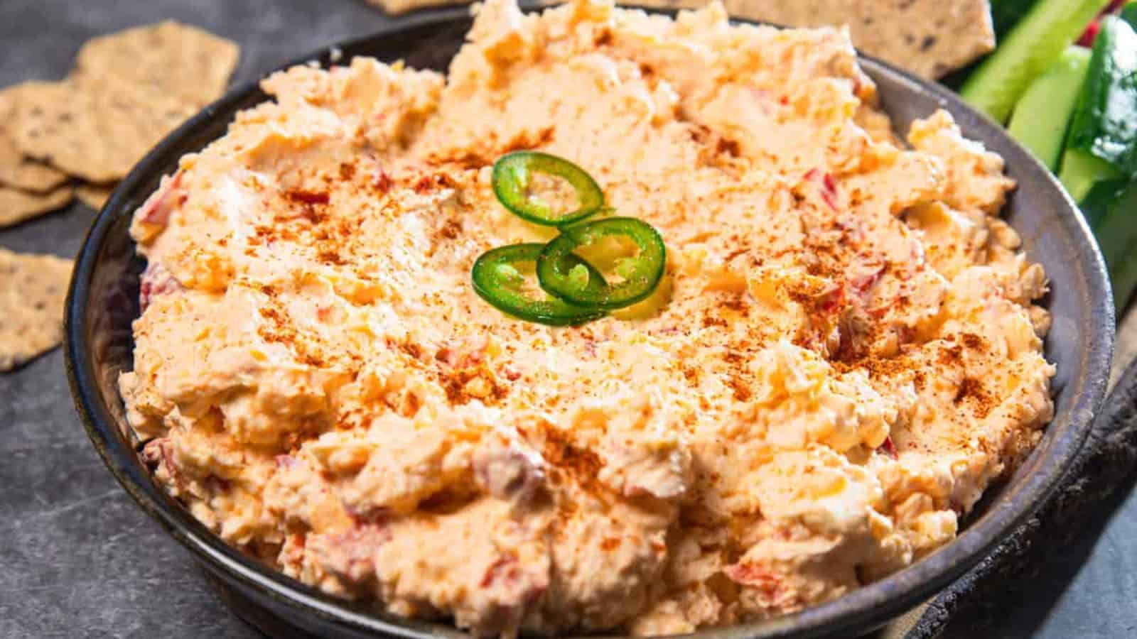 A bowl of creamy pimento cheese dip topped with sliced jalape&ntilde;os and a sprinkle of paprika.