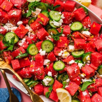 A platter of watermelon salad with cucumber, feta cheese, mint, and lemon slices on a pink table.