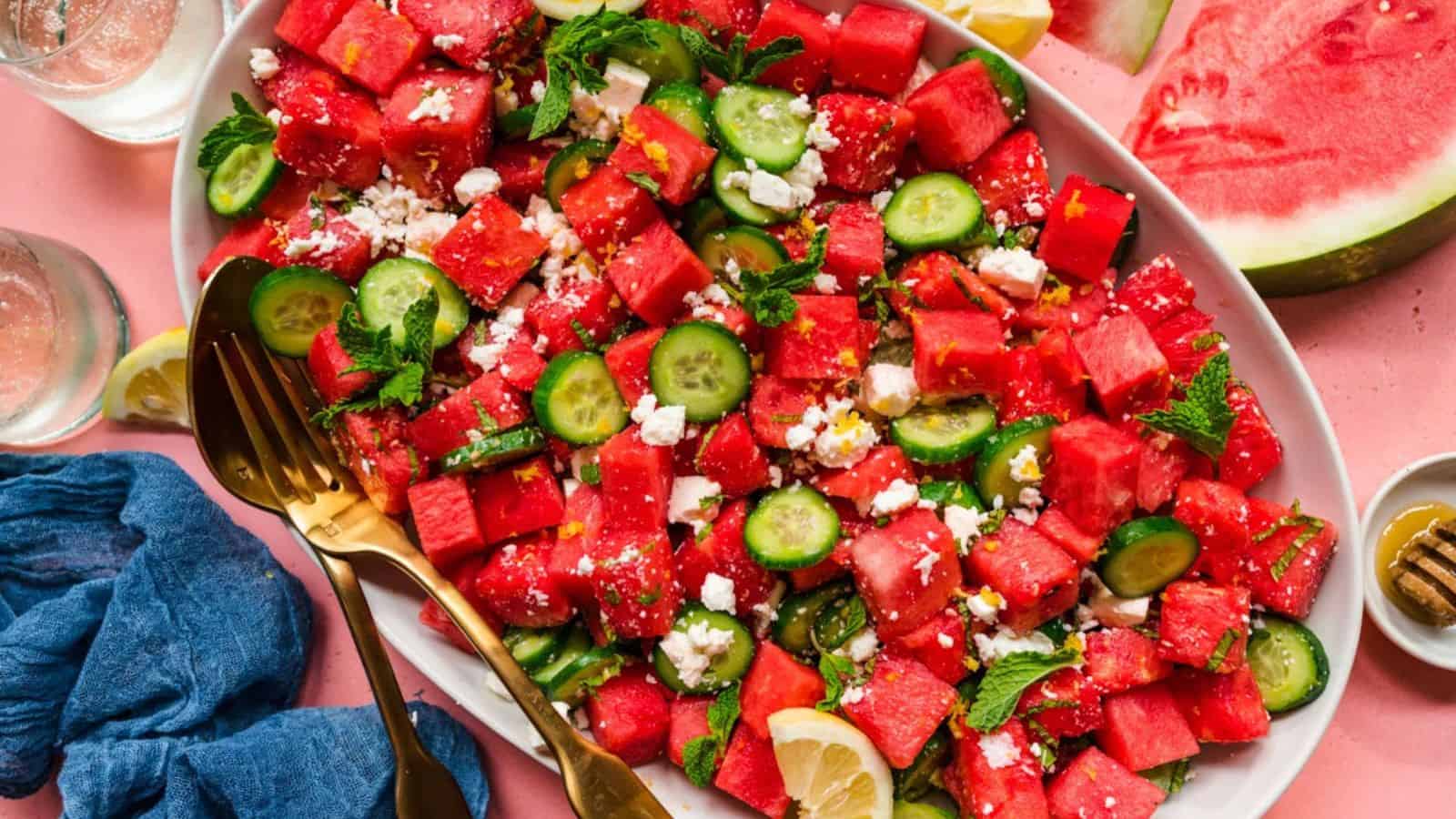 A platter of watermelon salad with cucumber, feta cheese, mint, and lemon slices on a pink table.
