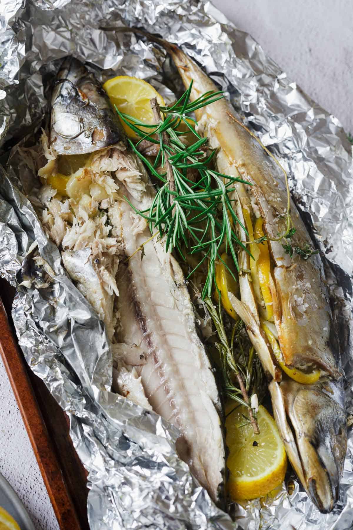 Two baked fish in foil with lemon slices and rosemary sprigs, partially filleted to show the inside.