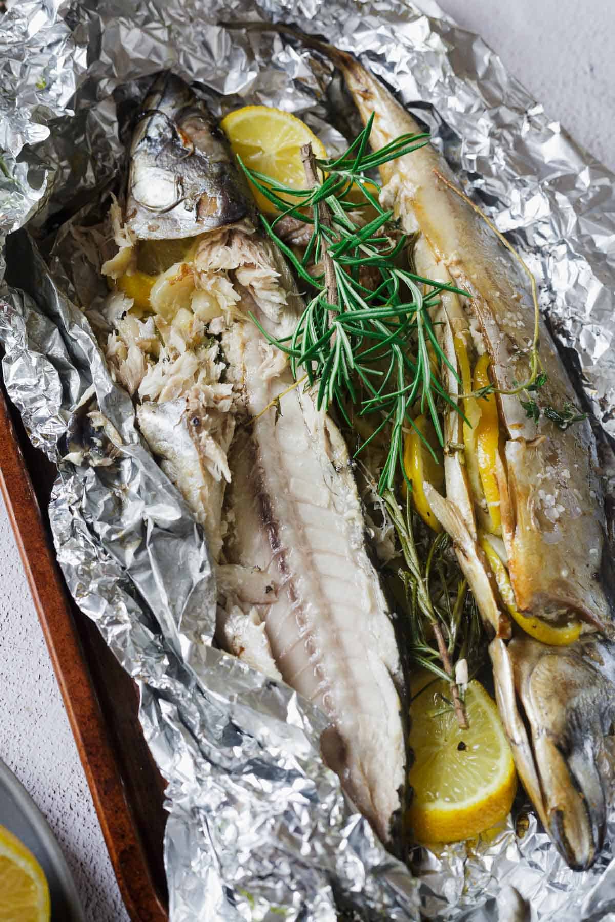 Two baked fish on foil garnished with lemon slices and fresh rosemary.