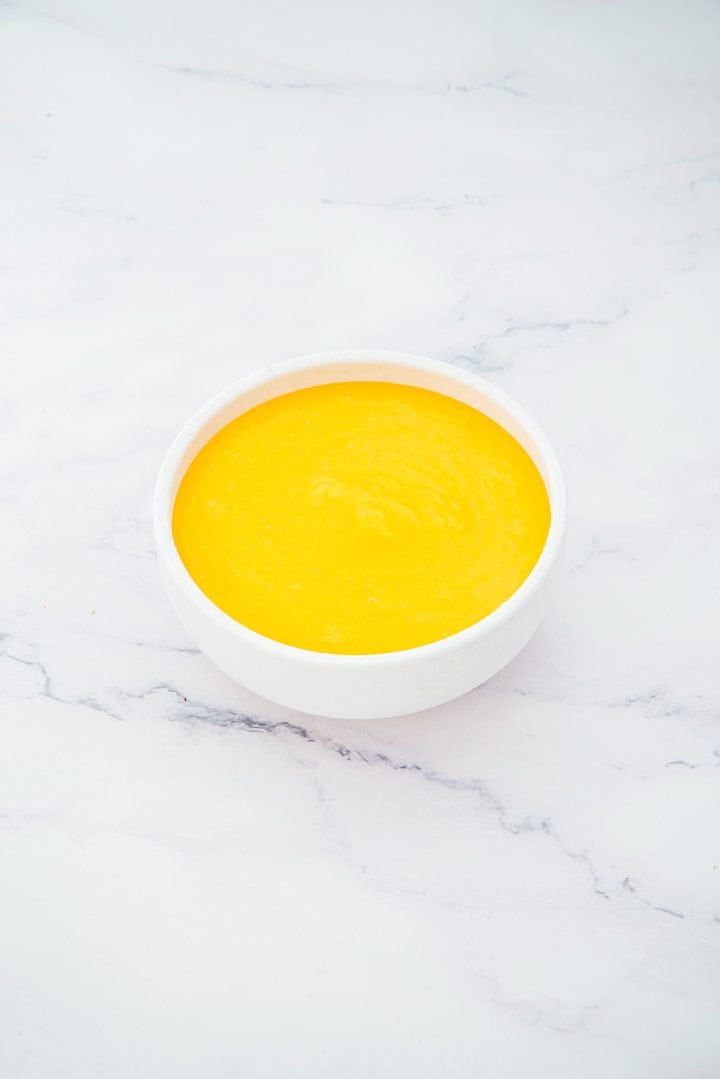 A white bowl filled with smooth, bright yellow mango puree on a white marble surface-perfect as a vibrant layer in Lemon Cheesecake Trifle Cups.