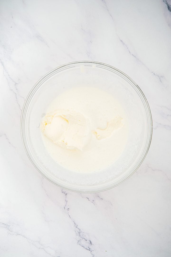 A glass bowl with cream and mascarpone cheese on a white marble surface, perfect for creating Lemon Cheesecake Trifle Cups.