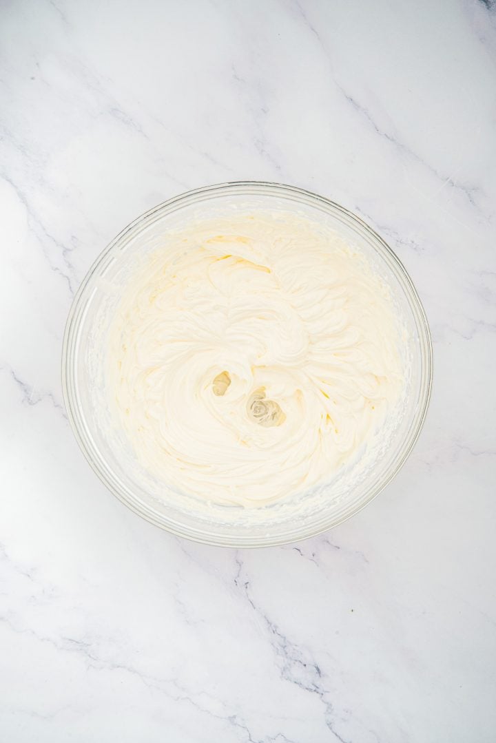 Glass bowl filled with whipped cream cheese on a white marble surface, seen from above-perfect for layering into delicious Lemon Cheesecake Trifle Cups.