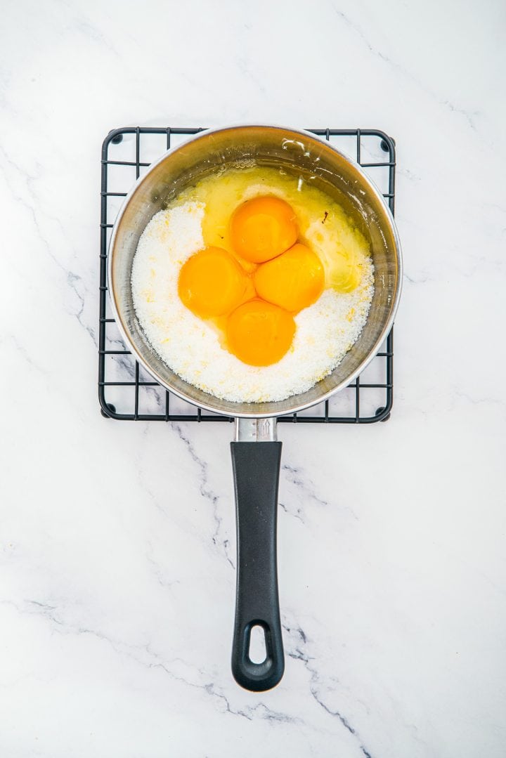 A saucepan with four raw eggs and sugar on a cooling rack, seen from above on a marble surface-perfect ingredients for starting delicious desserts like Lemon Cheesecake Trifle Cups.