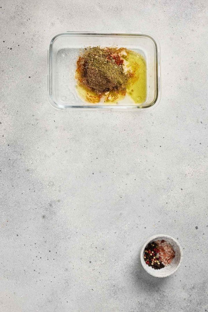 A glass dish with oil and spices, and a small bowl of pepper and salt on a light gray surface.