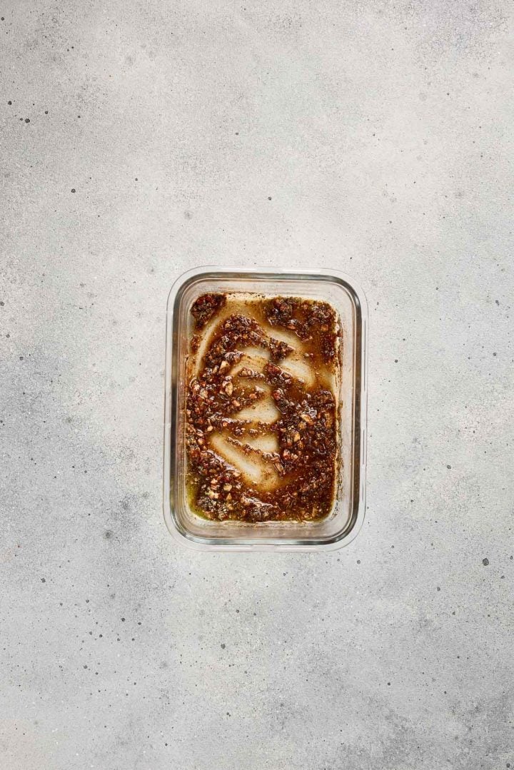 A glass container with a small amount of marinade residue on a light gray surface.