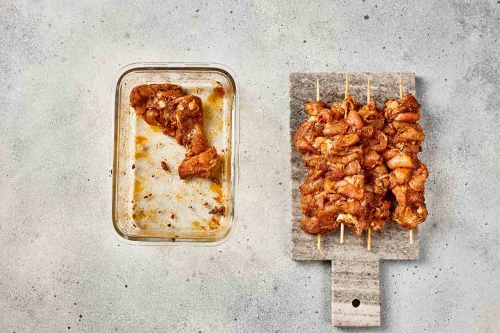 Marinated pieces of chicken on skewers beside a glass dish with leftover marinade.