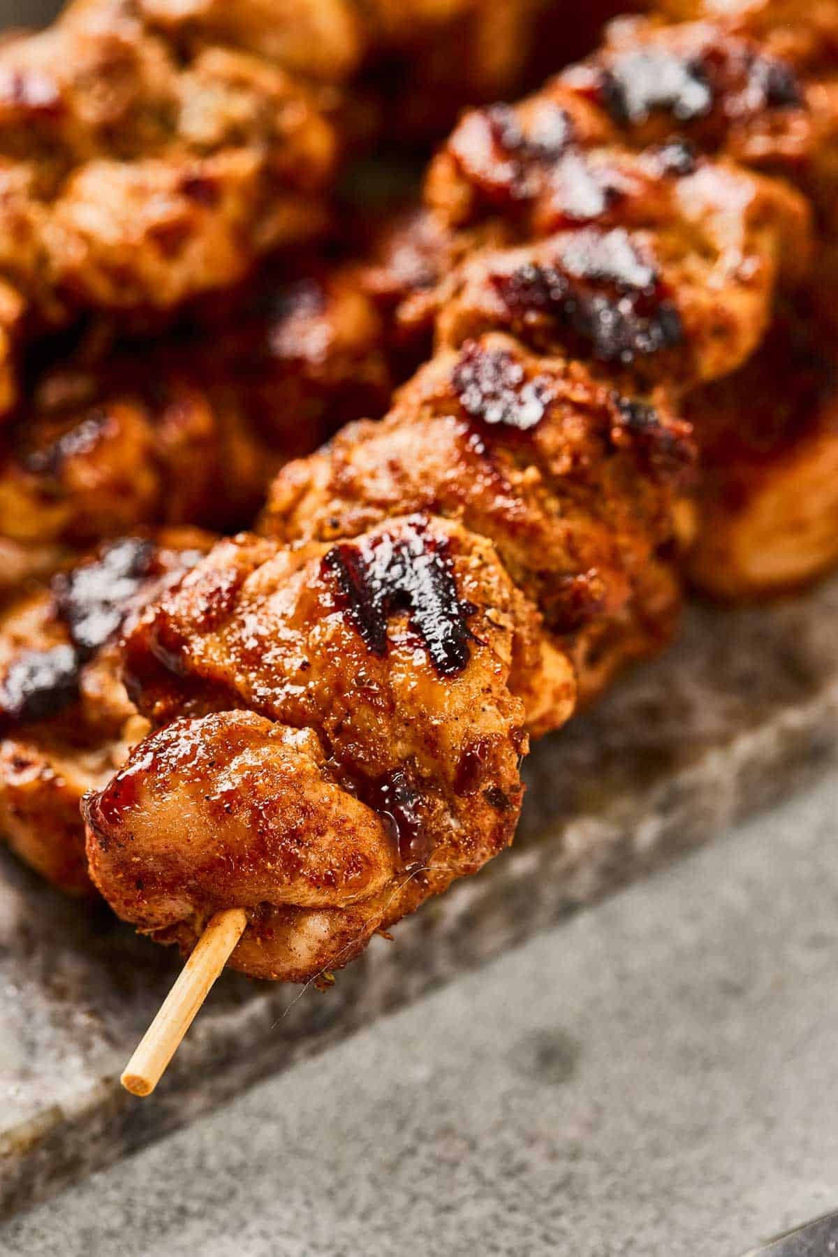 Grilled chicken kebab on a skewer with visible char marks, served on a stone surface.