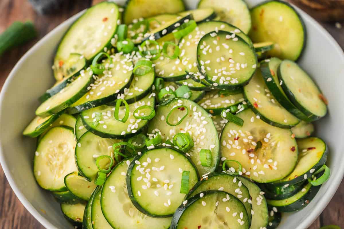Sliced cucumber salad topped with sesame seeds and chopped green onions in a white bowl.