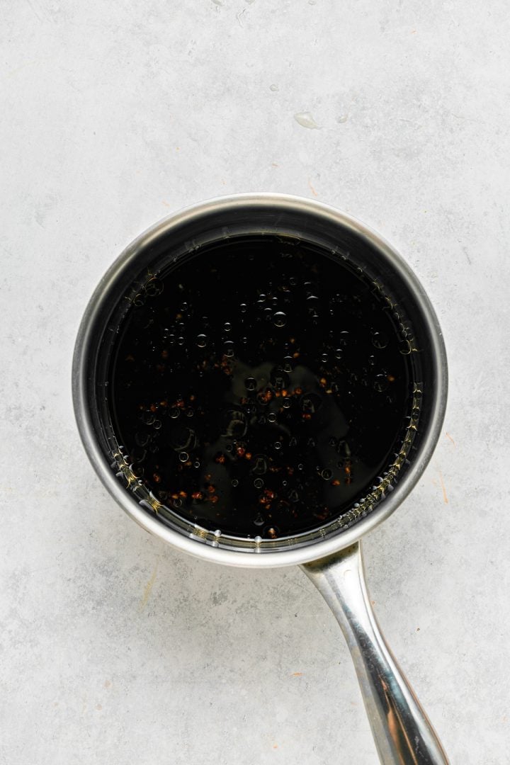 A small stainless steel saucepan filled with a dark liquid sits on a light gray surface.