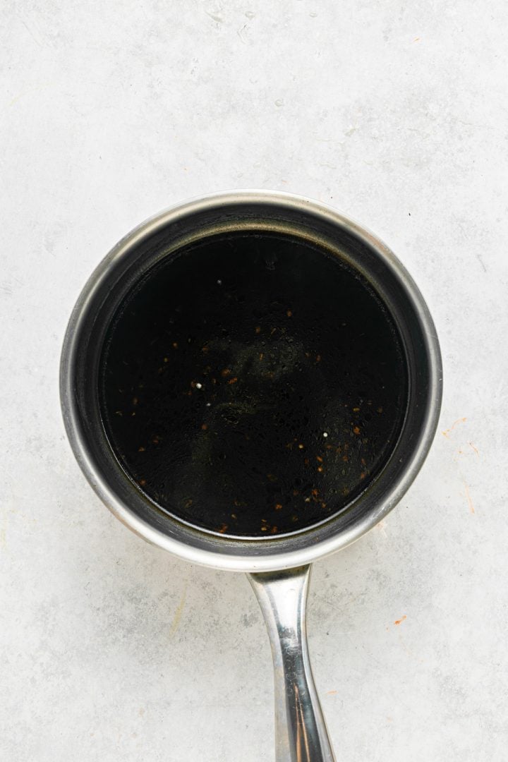 A small stainless steel saucepan filled with a dark liquid, viewed from above on a light gray surface.