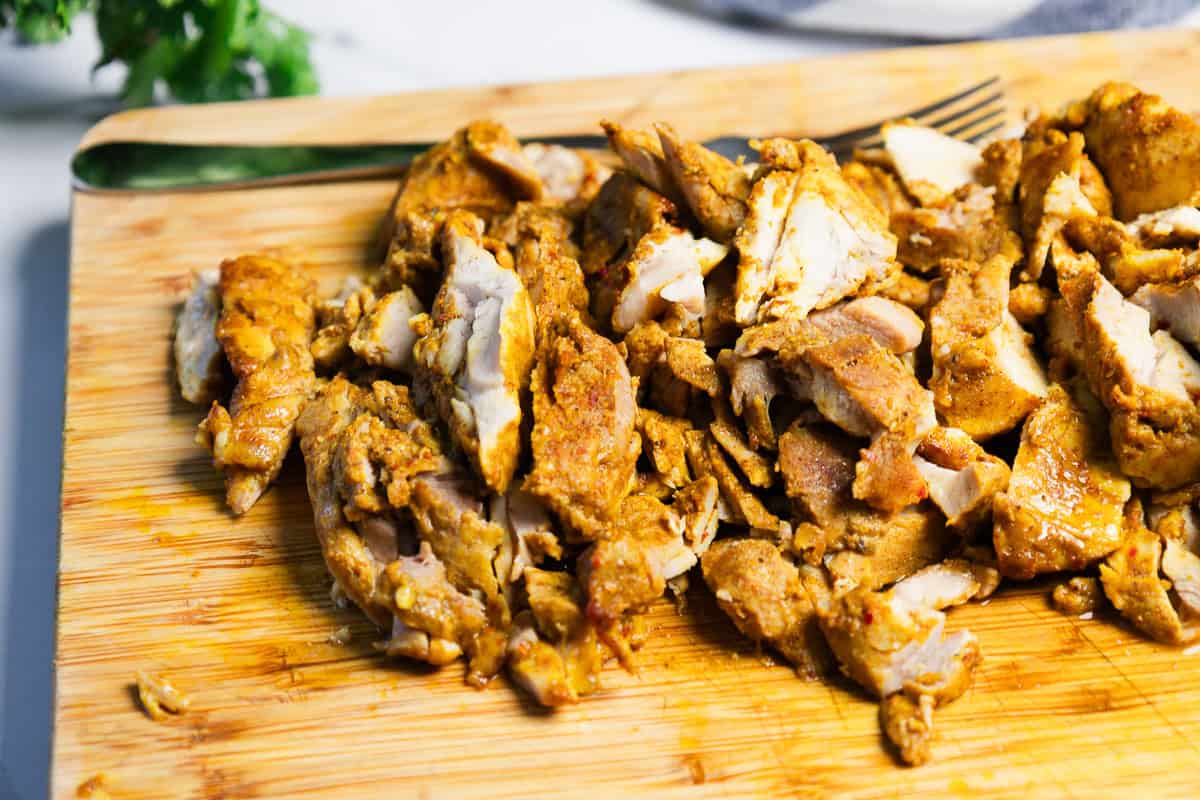 Sliced seasoned cooked chicken on a wooden cutting board with a fork in the background.