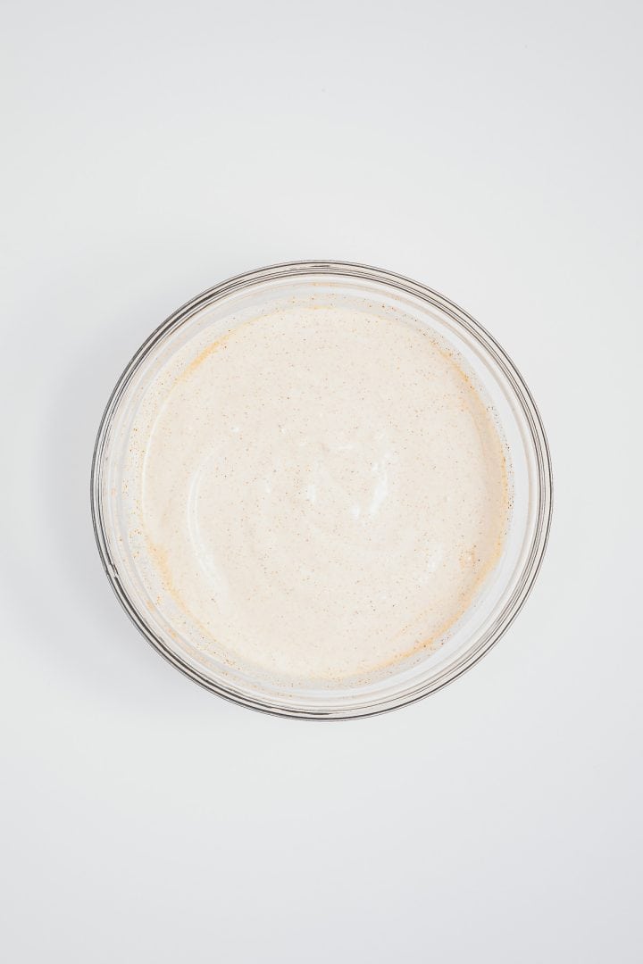 A clear glass bowl filled with a creamy, light beige sauce-perfect for drizzling over Mexican street corn elotes-on a white background.