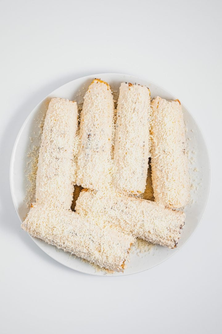 Six coconut-covered dessert rolls arranged on a white plate against a white background, inspired by the bold flavors of Mexican street corn elotes.