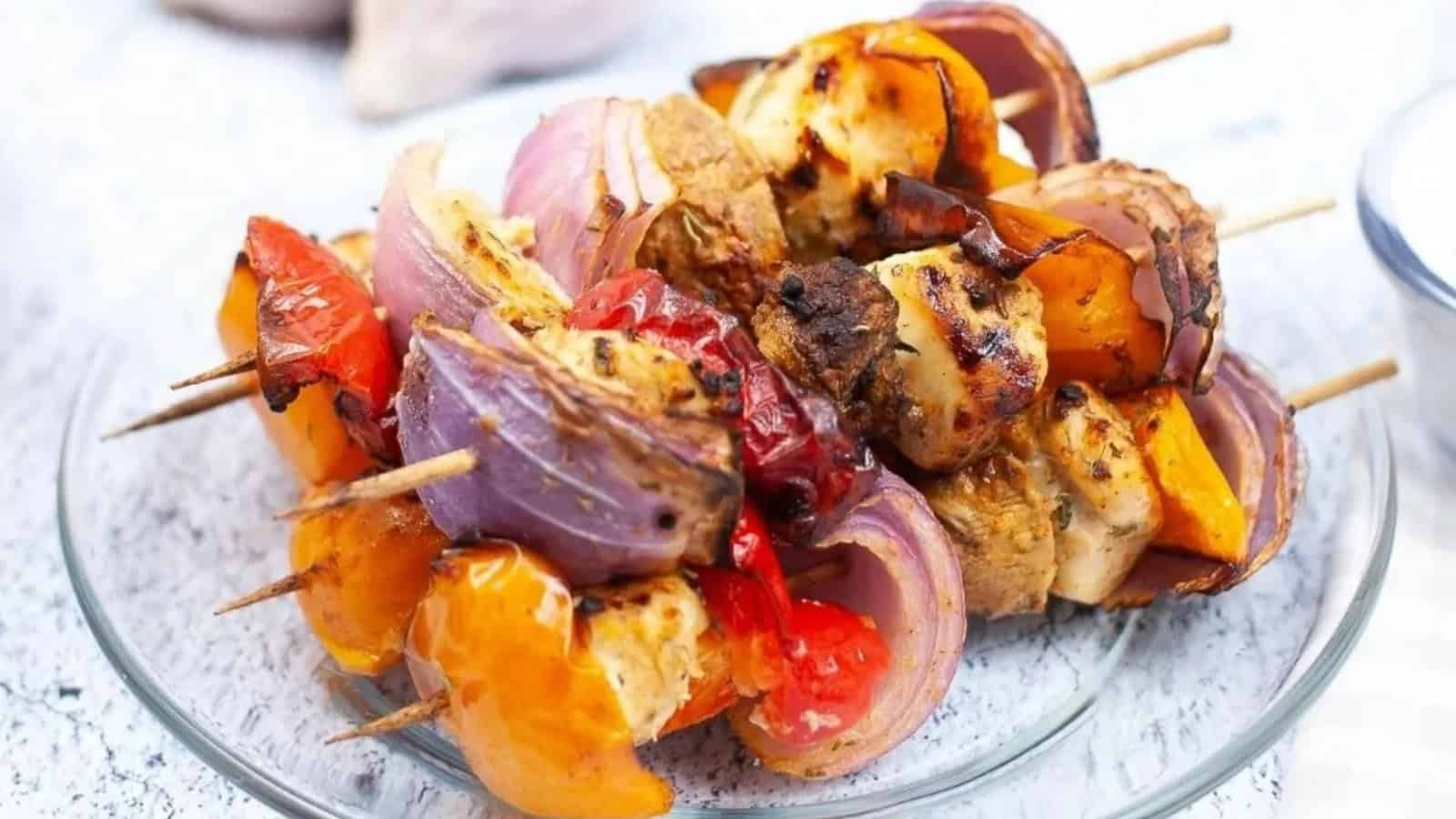 Colorful grilled vegetable and chicken skewers on a clear glass plate, featuring peppers, onions, and tomatoes.