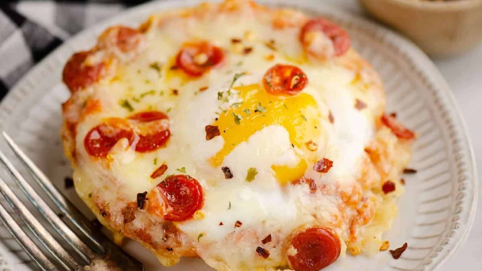 A baked egg on a mini pizza with melted cheese and pepperoni on a white plate with a fork.