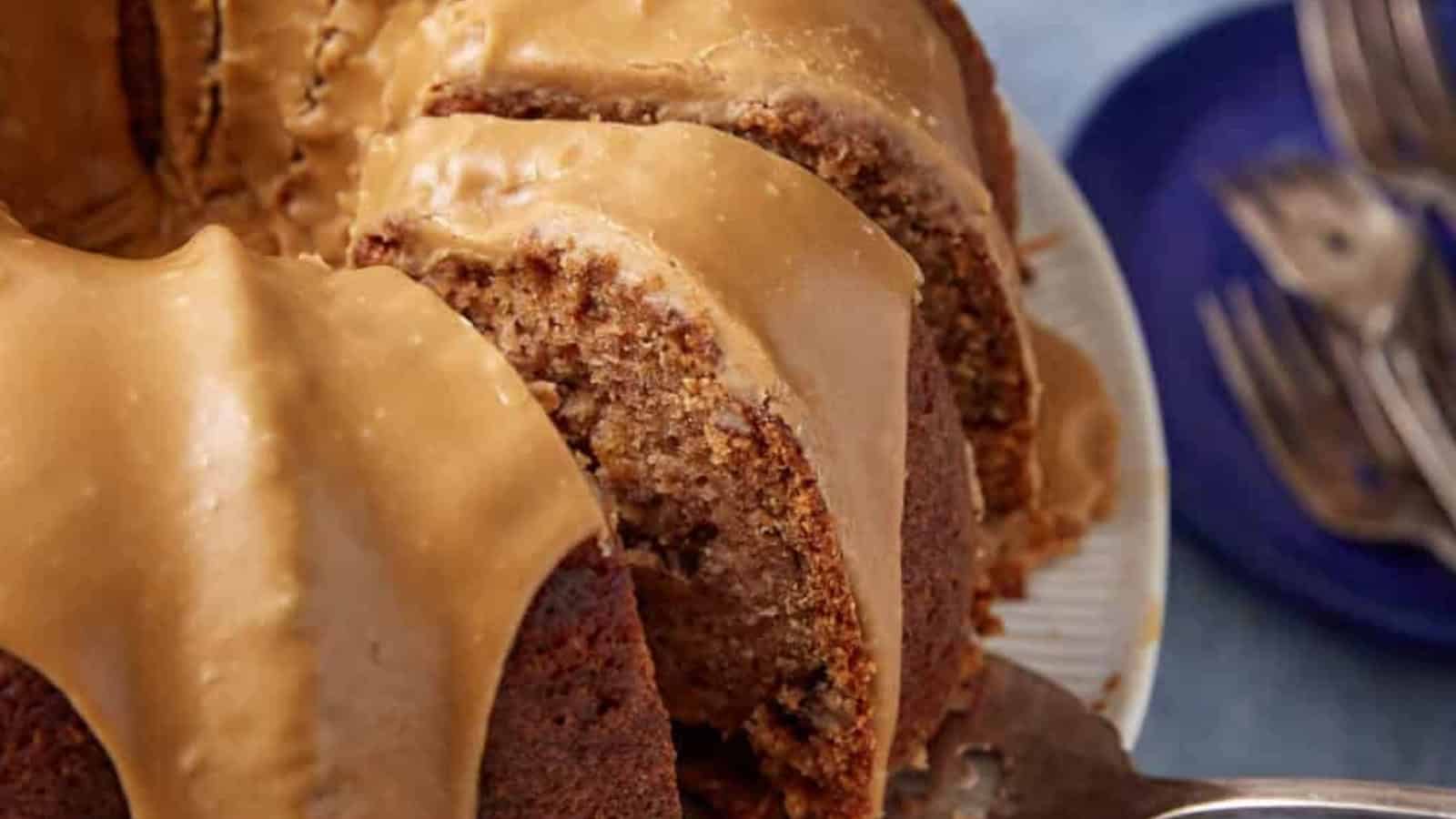 A sliced bundt cake with caramel glaze on top, served on a plate with a blue dish and forks nearby.