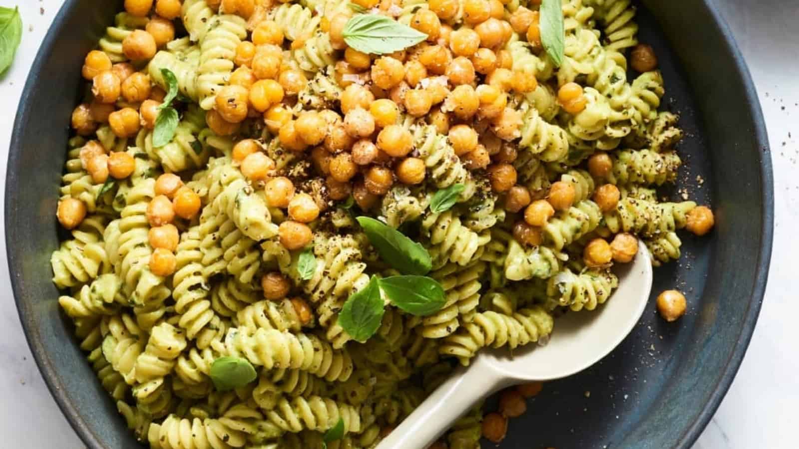Rotini pasta with creamy green sauce, crispy chickpeas, and fresh basil in a black bowl with a spoon.