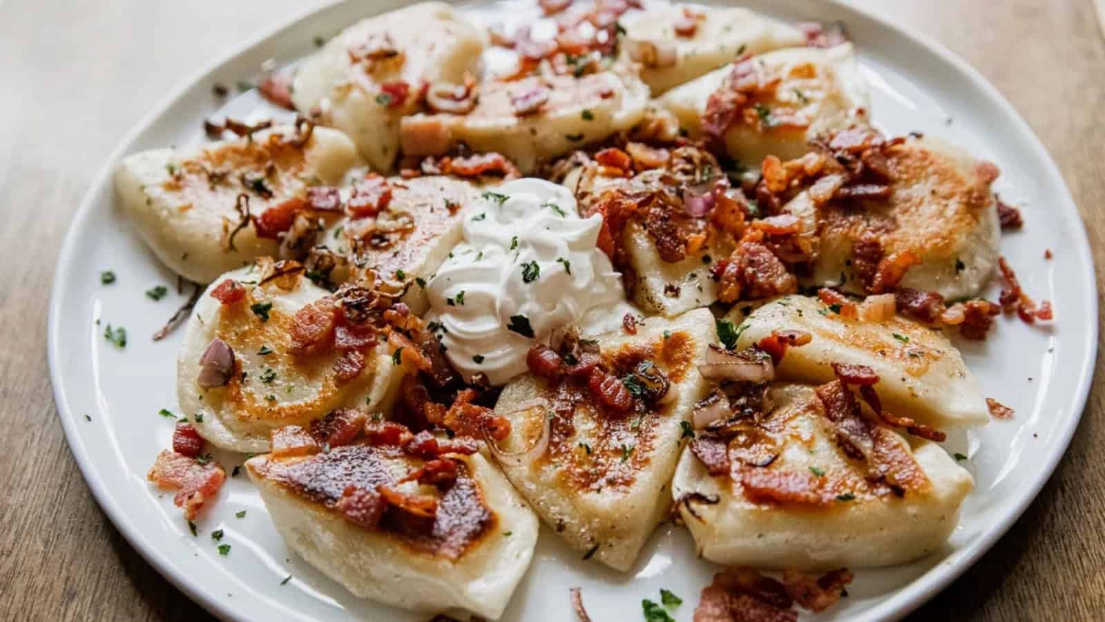 A plate of pierogies topped with crispy bacon, saut&eacute;ed onions, herbs, and a dollop of sour cream.