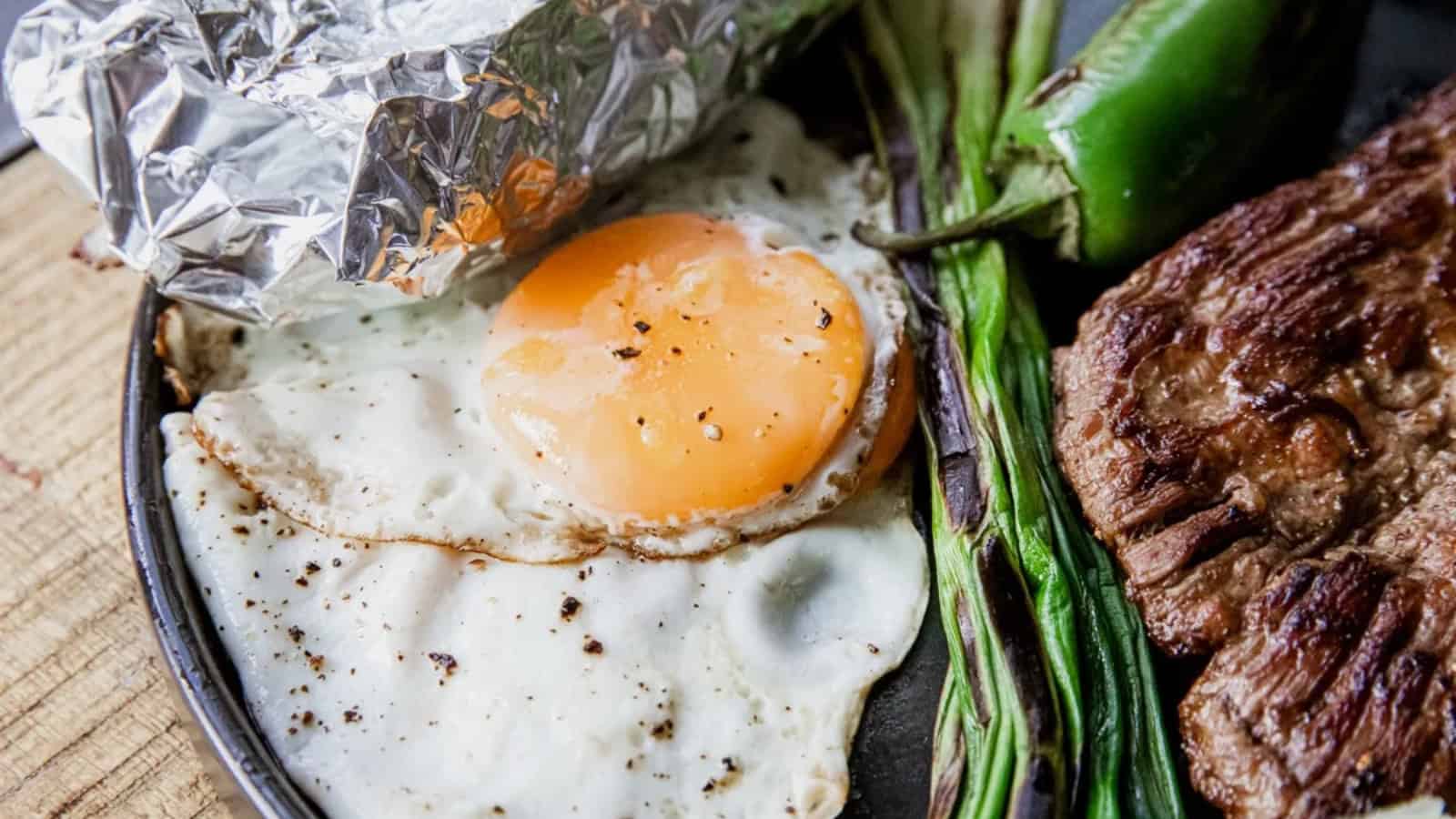 Fried egg, grilled steak, green onions, a jalapeño, and foil-wrapped food on a plate.
