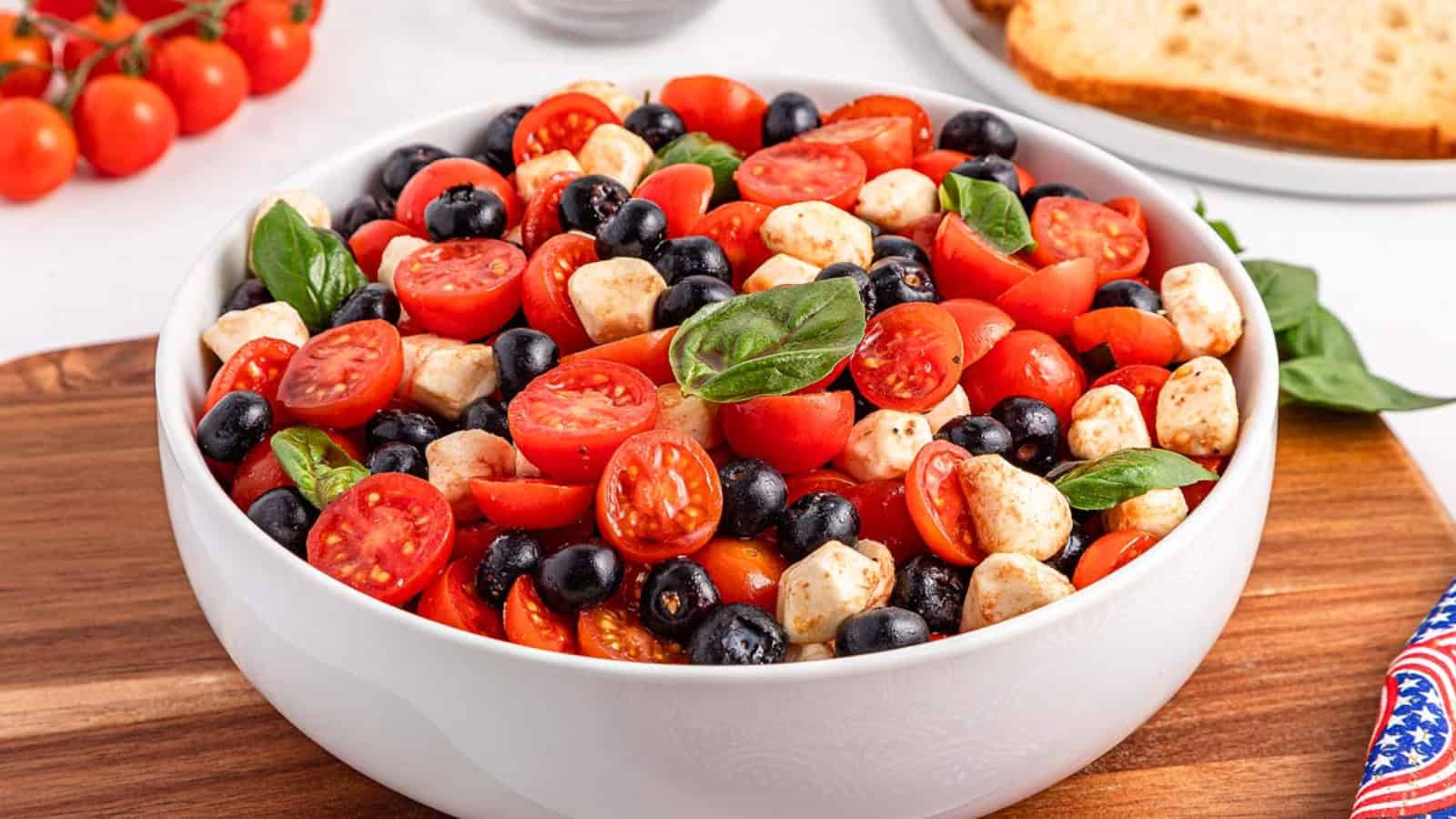 Blueberries, sliced tomatoes, and mozzarella pieces are arranged together with green leaves on a plate.