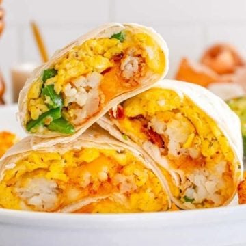 Three breakfast burritos with eggs, cheese, hashbrowns, and jalapenos, served with tater tots and avocado.