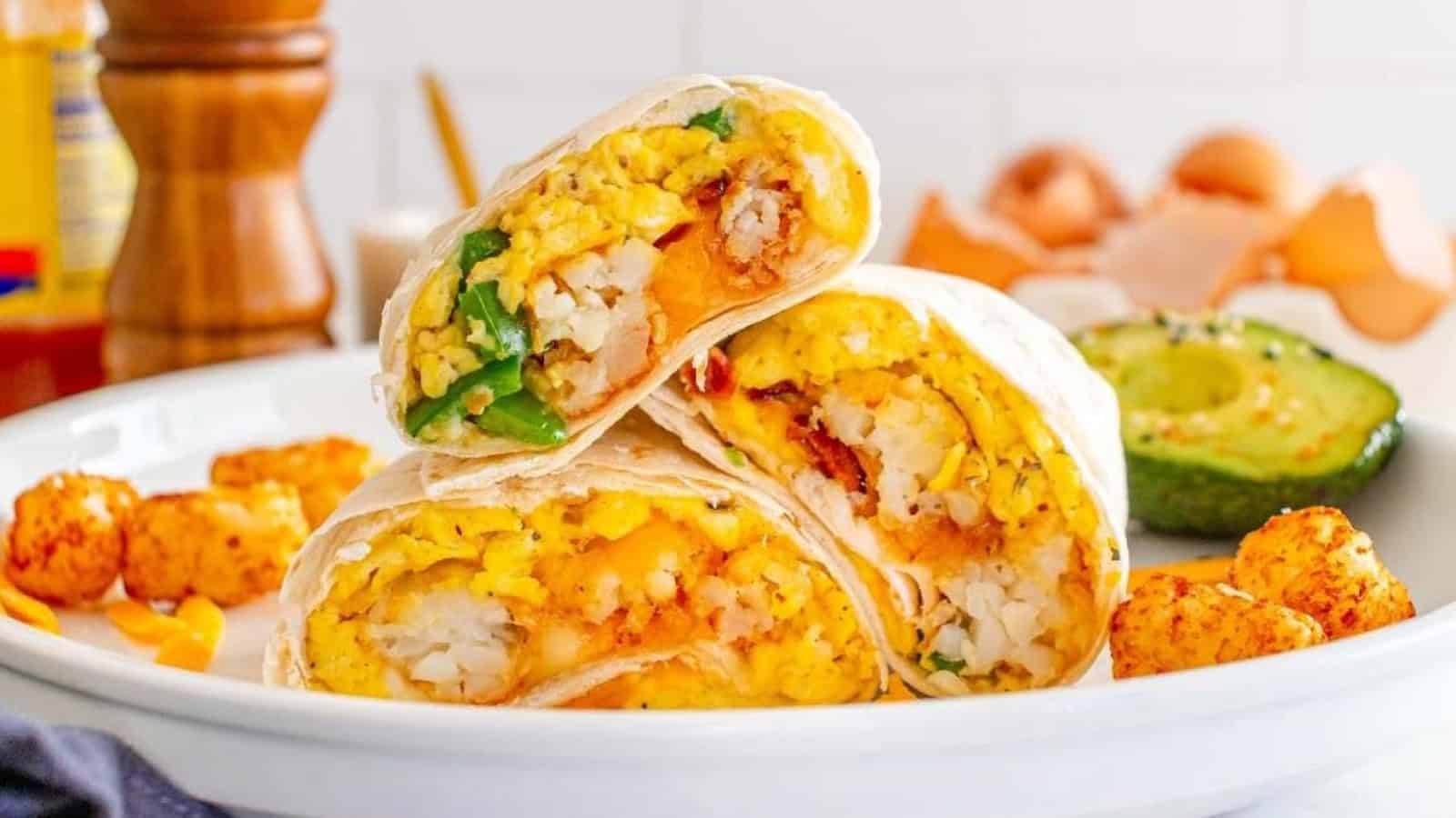 Three breakfast burritos with eggs, cheese, hashbrowns, and jalapenos, served with tater tots and avocado.