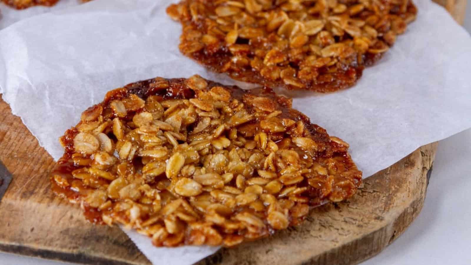 Oatmeal lace cookies on parchment paper atop a wooden board.
