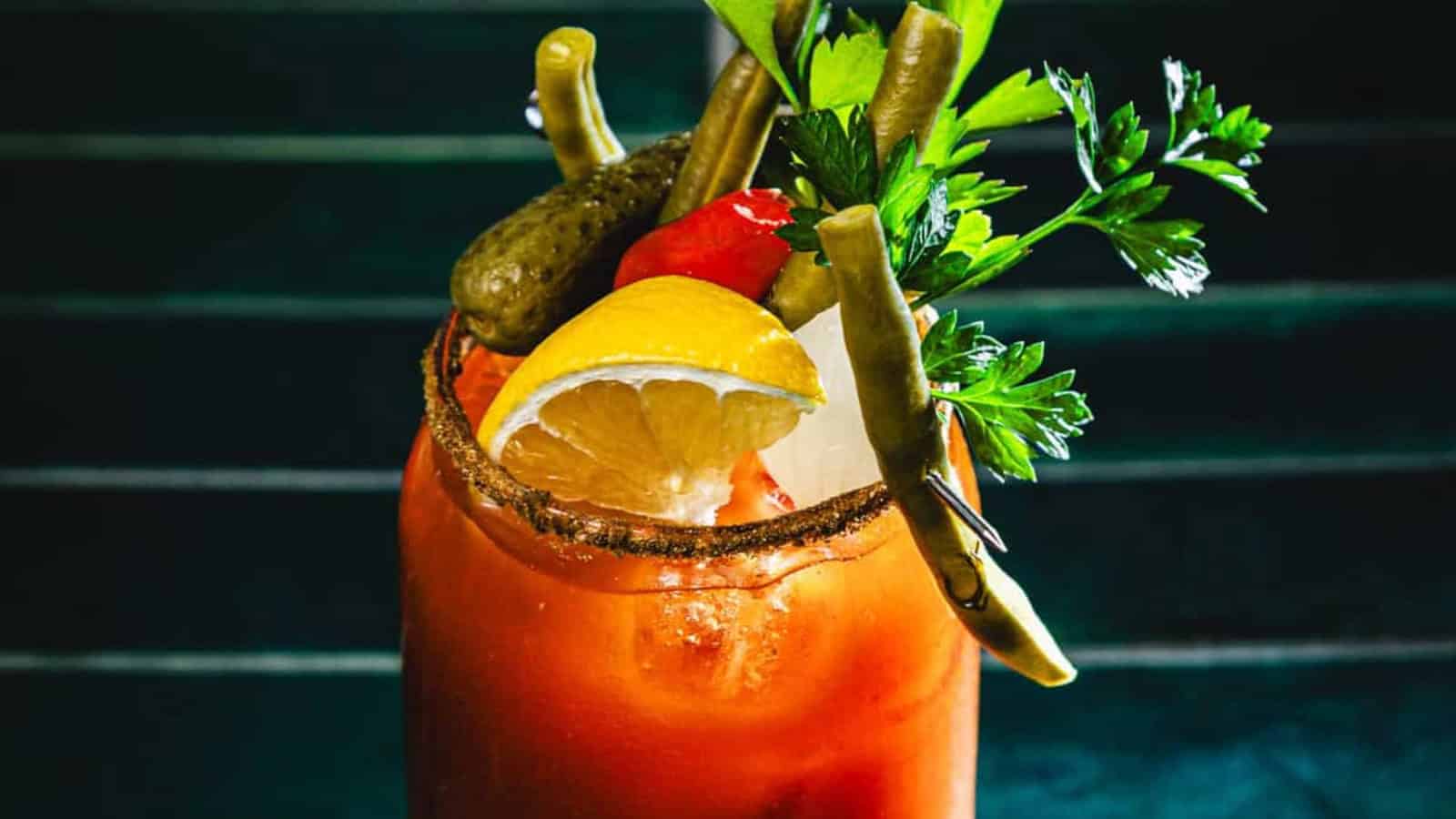 Bloody Mary cocktail garnished with lemon, pickles, green beans, parsley, and a spiced rim, close up.