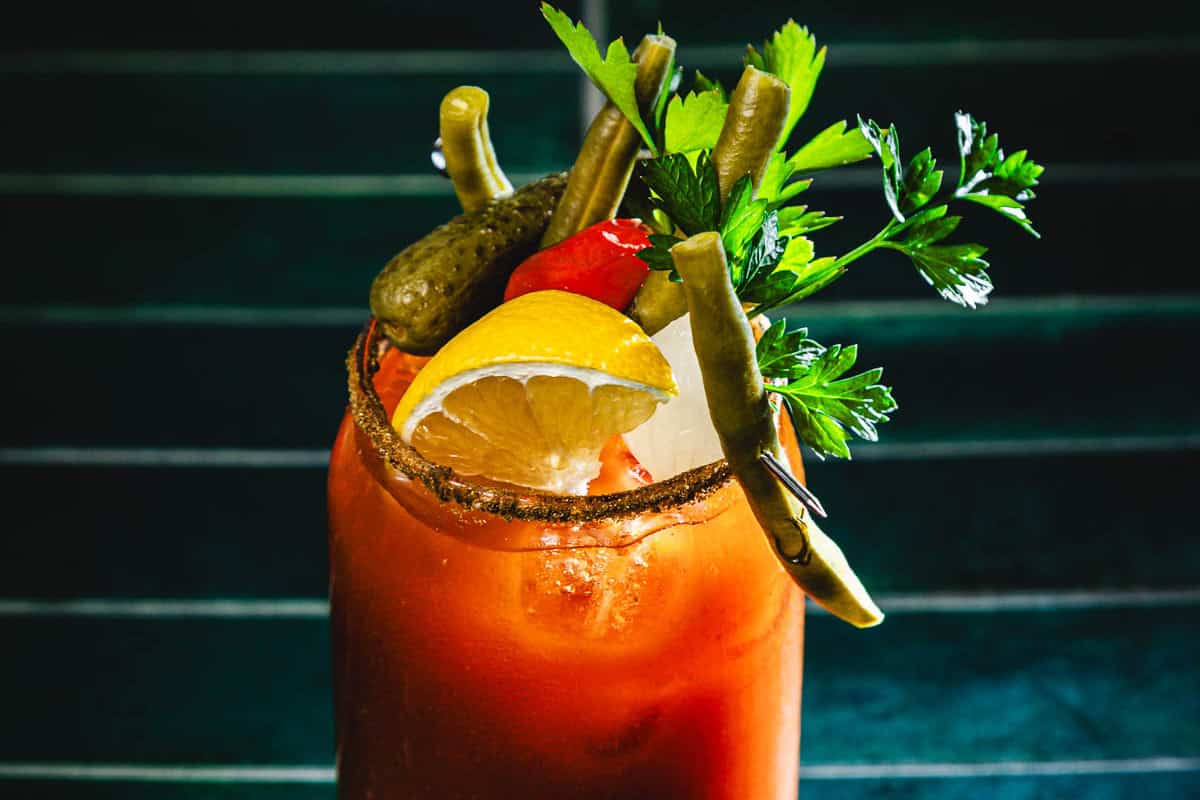 Bloody Mary cocktail with ice, lemon, pickles, green beans, parsley, and other garnishes in a rimmed glass&mdash;this classic drink is also known as a Caesar Cocktail in some regions, offering a savory twist perfect for brunch.