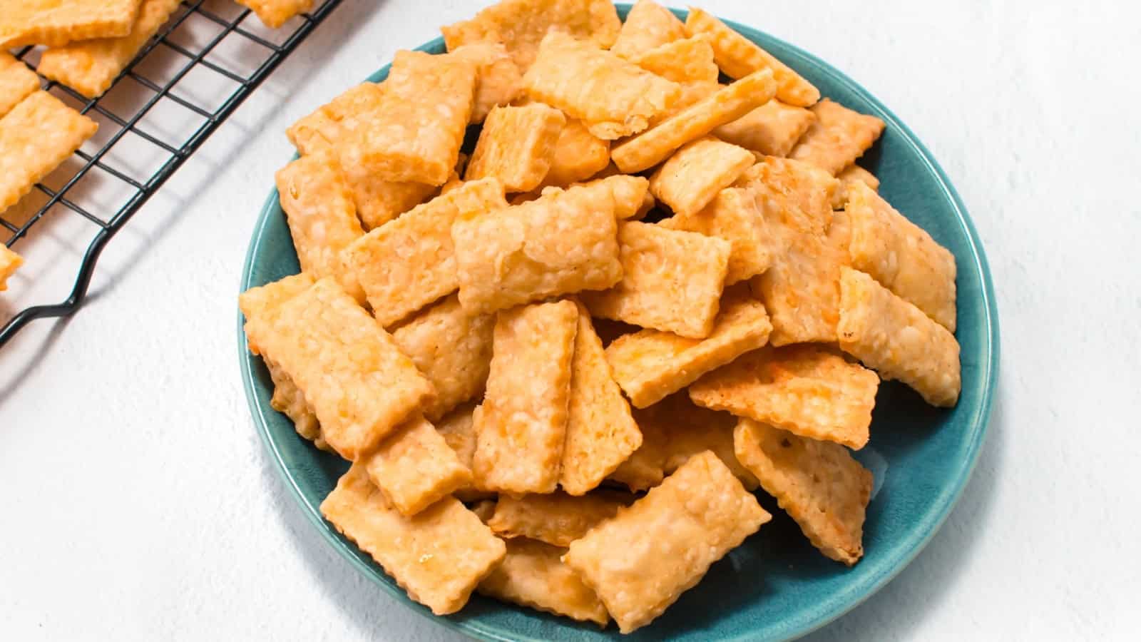 A teal plate filled with square, golden baked cheese crackers on a white surface.