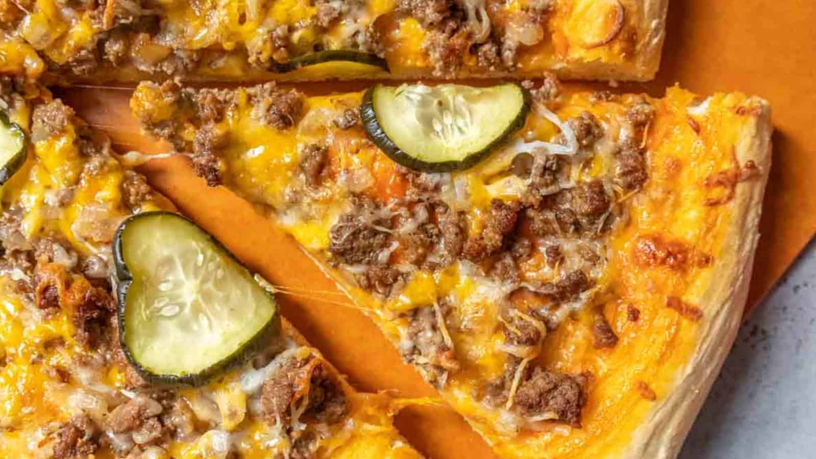 Close-up of cheeseburger pizza slices topped with ground beef, cheese, and pickles on a crust.