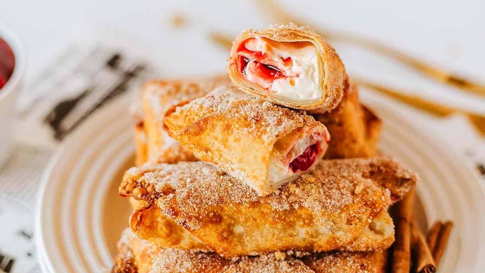 Plate of sugar-dusted fried pastry rolls filled with cream and strawberry filling, with one roll cut open.