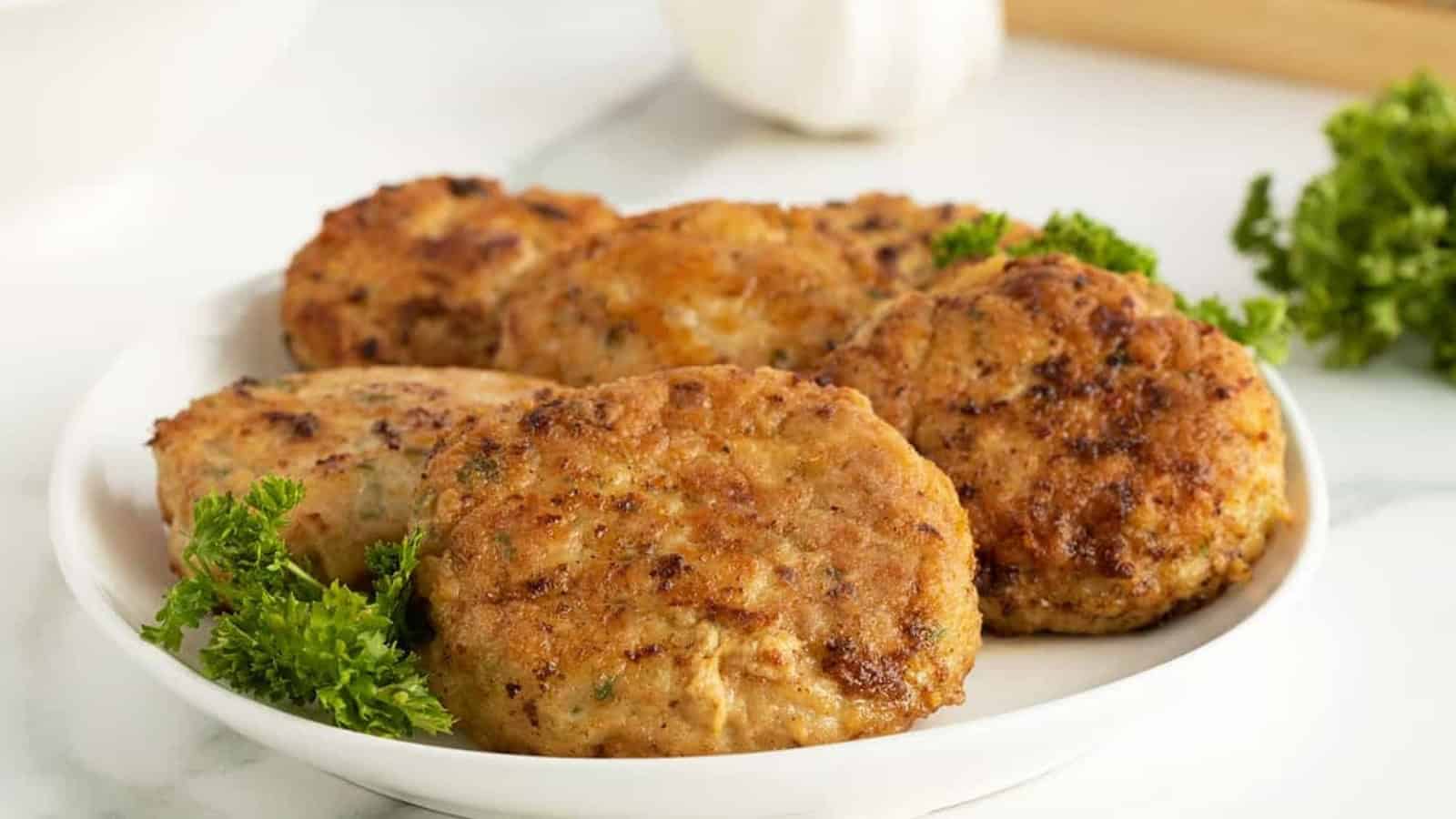 Five golden-brown chicken patties on a white plate, garnished with fresh parsley.