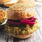A chickpea burger with pickled red onions on a sesame bun, set on a wooden surface.