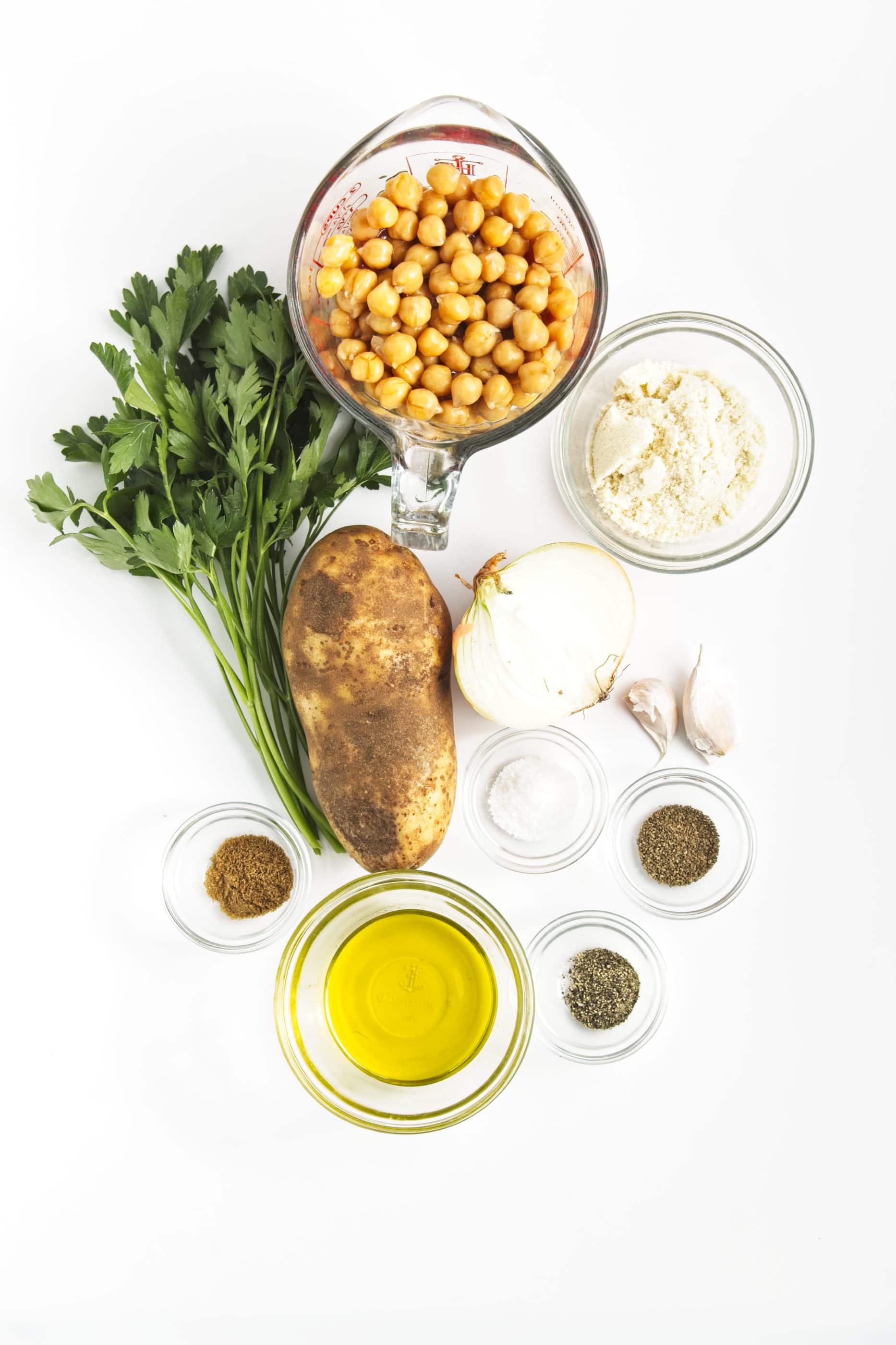 Chickpeas, parsley, potato, onion, flour, garlic, oil, and spices—perfect ingredients for delicious chickpea burgers—are arranged on a white background.