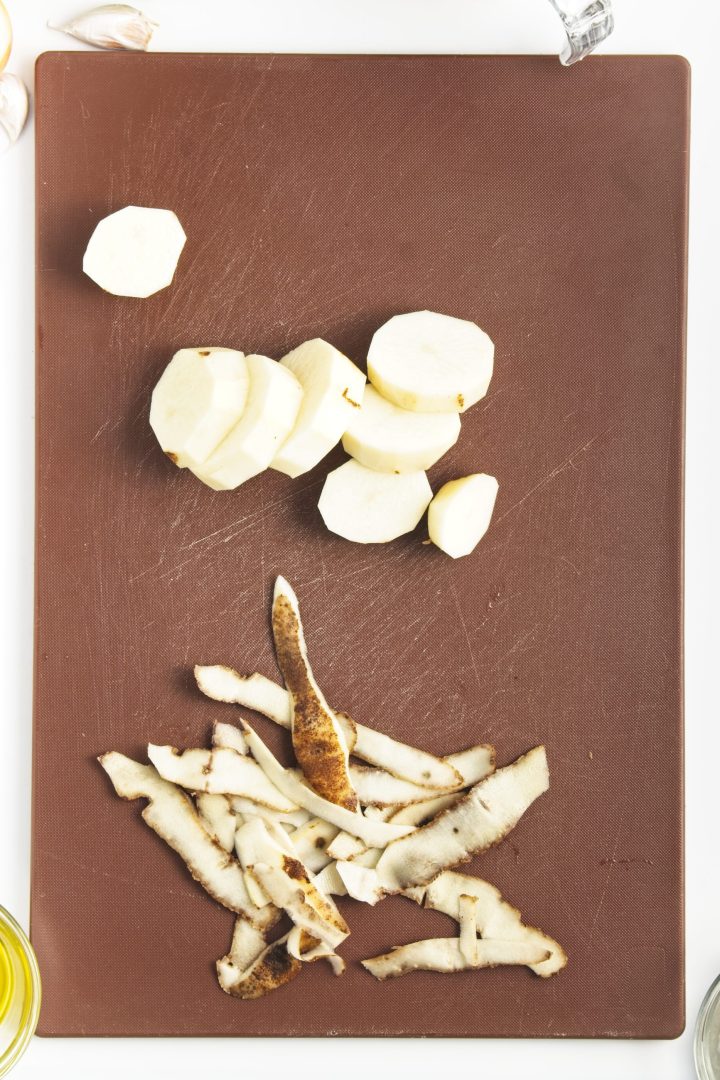 Peeled and sliced potatoes with potato peels on a brown cutting board, ready for your next recipe-perfect as a side for homemade chickpea burgers.