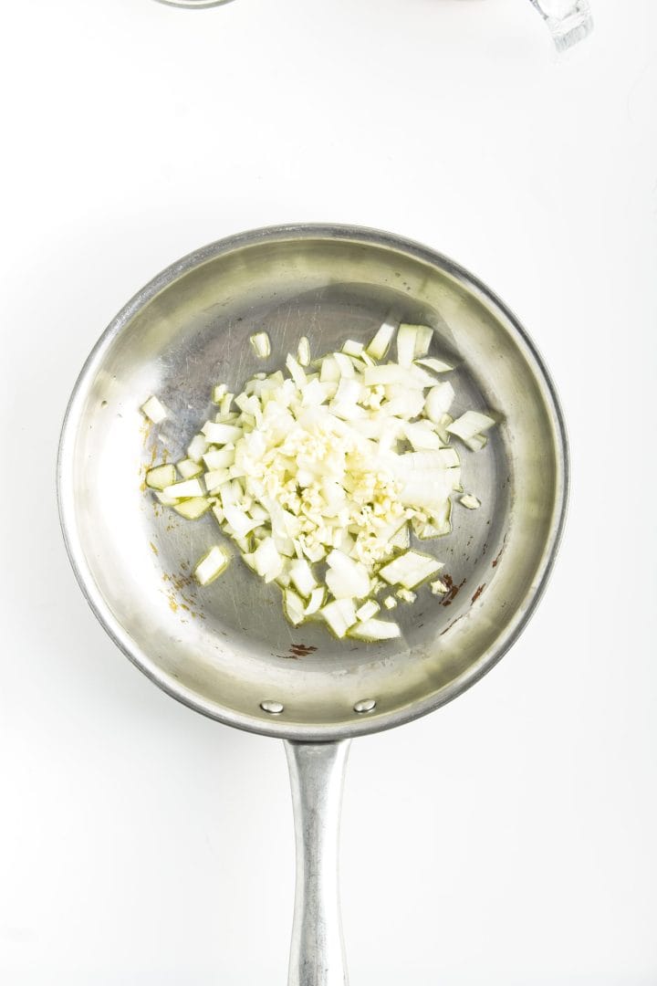 Chopped onions and garlic in a stainless steel frying pan on a white background-perfect for starting your favorite chickpea burgers recipe.
