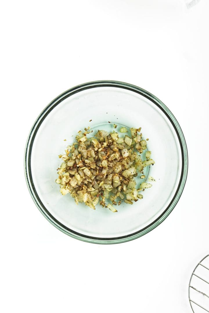 Chopped, sautéed onions with spices—perfect as a flavorful topping or mix-in for chickpea burgers—in a clear glass bowl on a white background.