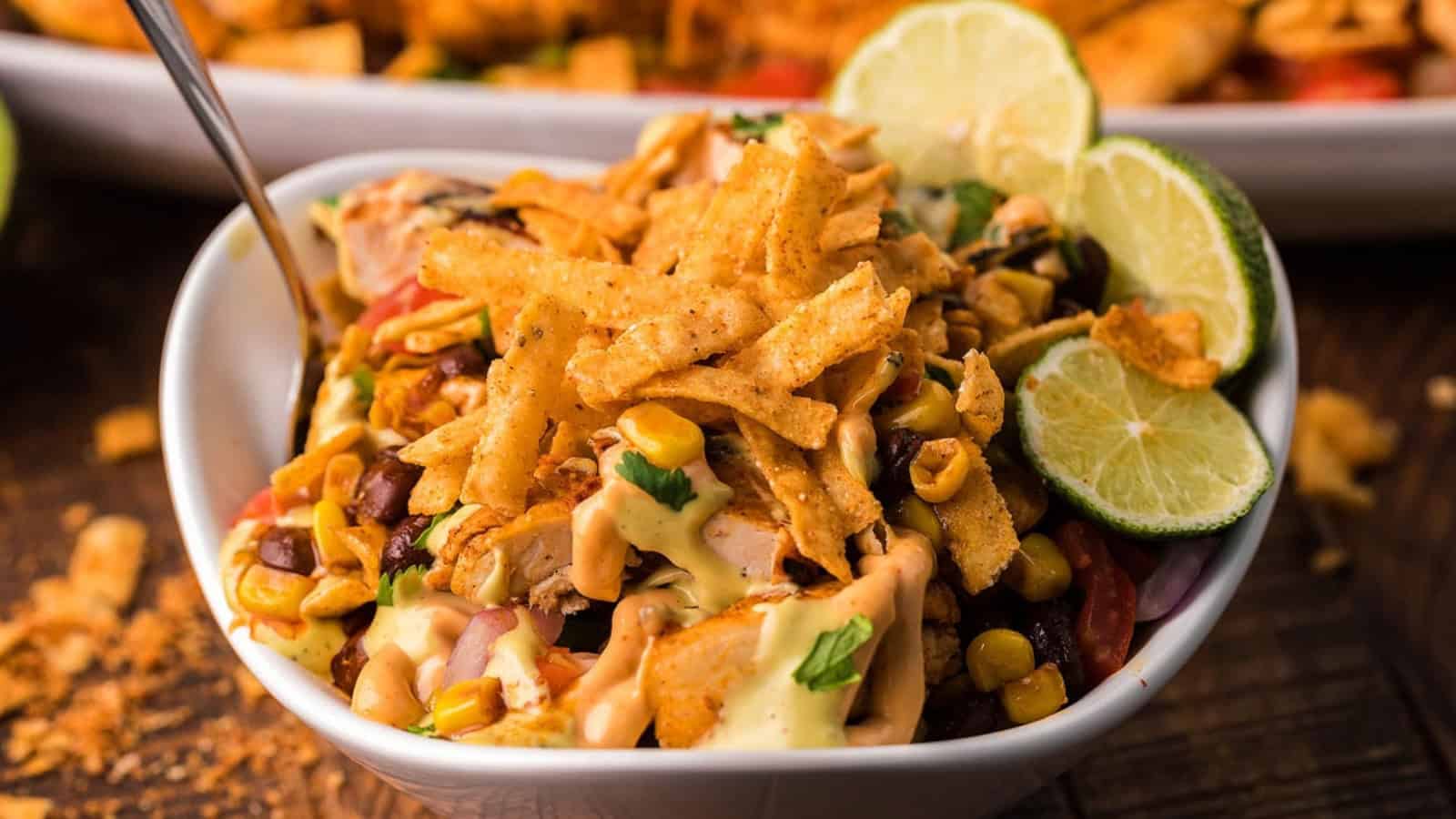 Bowl of southwest chicken salad topped with crispy tortilla strips, corn, and lime slices.