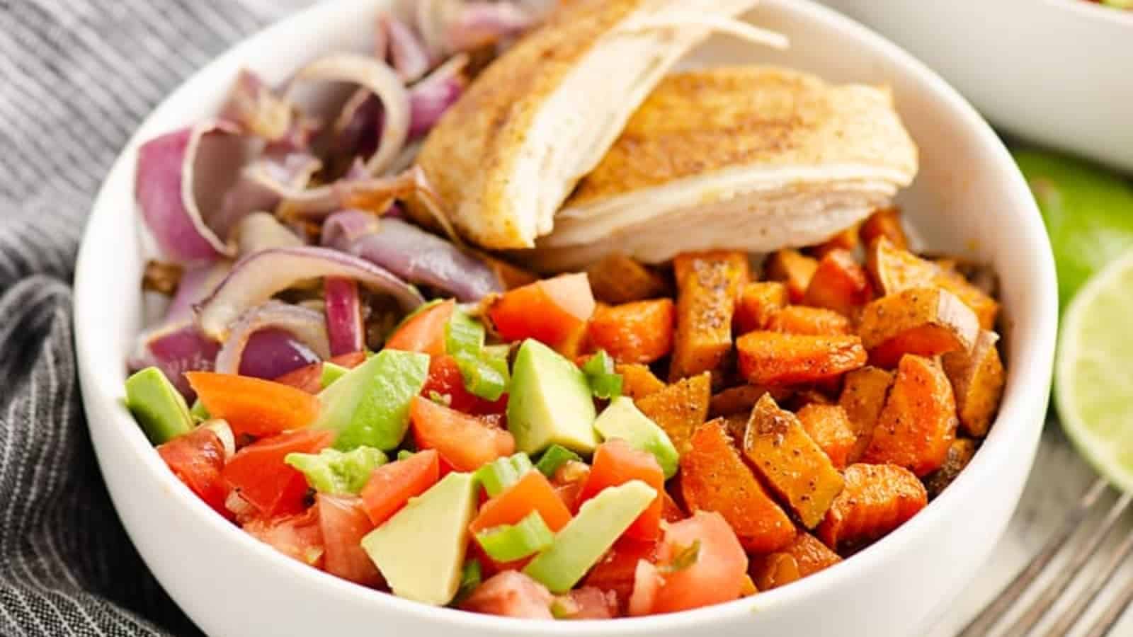 A bowl with grilled chicken, roasted sweet potatoes, avocado, tomatoes, and saut&eacute;ed red onions.