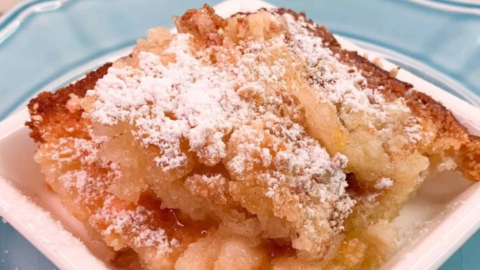 A square of apple cobbler topped with powdered sugar on a white dish, placed on a light blue plate.